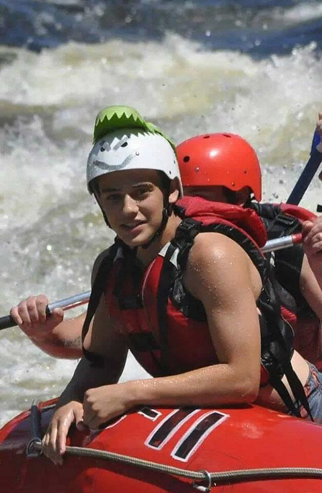 Nolan smiling while whitewater rafting, wearing a helmet and life jacket